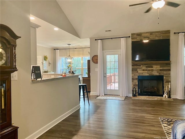 living area featuring dark wood-style flooring, visible vents, vaulted ceiling, and a fireplace