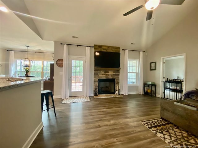 living area featuring dark wood-style floors, a fireplace, lofted ceiling, visible vents, and ceiling fan with notable chandelier