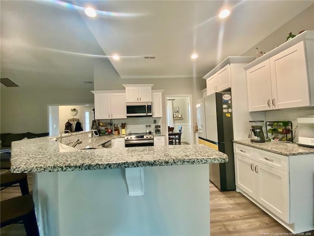 kitchen with a breakfast bar, stainless steel appliances, tasteful backsplash, white cabinetry, and a sink