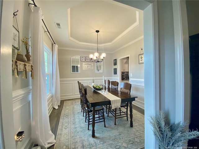 dining space with wood finished floors, visible vents, ornamental molding, wainscoting, and a raised ceiling