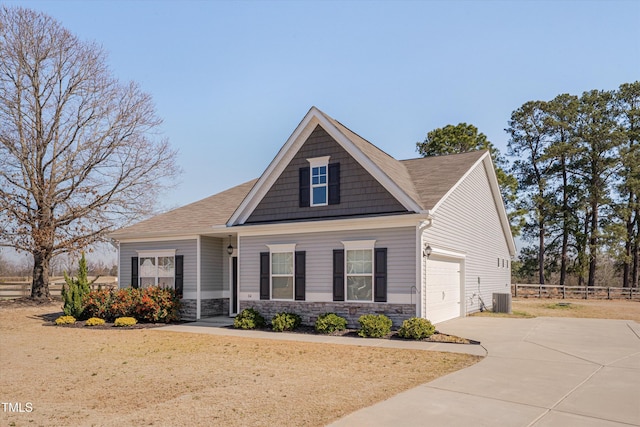 craftsman house with central air condition unit, an attached garage, fence, stone siding, and driveway