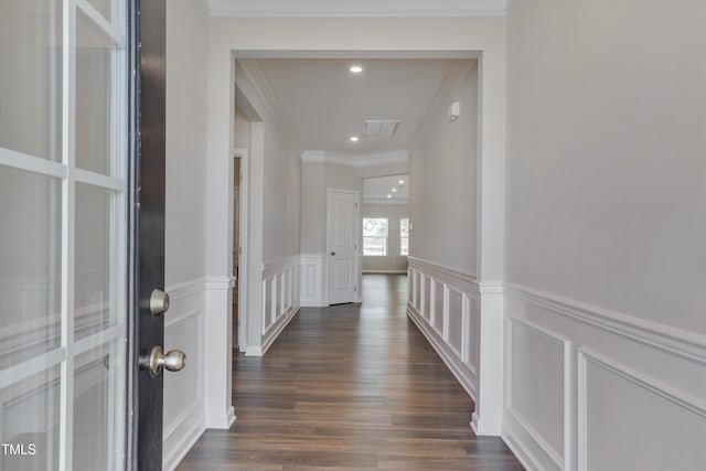 hallway with ornamental molding, dark wood-style flooring, wainscoting, and a decorative wall