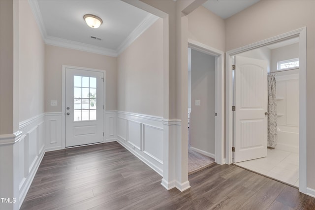 foyer entrance featuring a decorative wall, dark wood-style flooring, visible vents, ornamental molding, and wainscoting