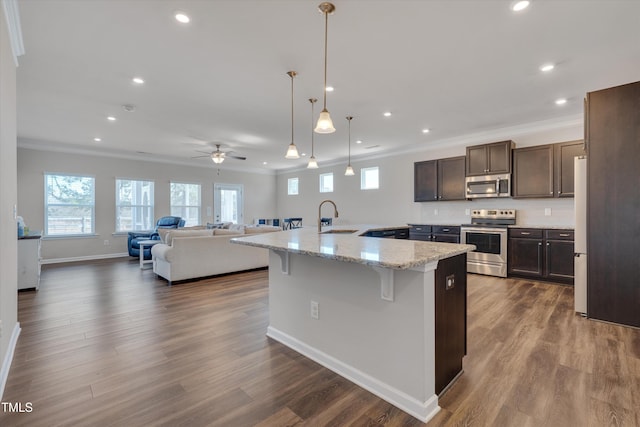 kitchen featuring dark brown cabinetry, dark wood-style flooring, a kitchen breakfast bar, ornamental molding, and appliances with stainless steel finishes