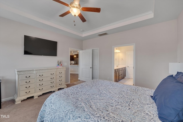 bedroom with a raised ceiling, light colored carpet, visible vents, ensuite bathroom, and baseboards