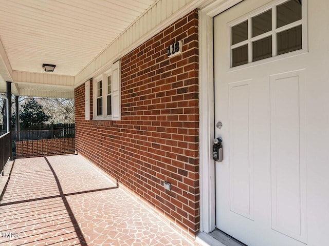 doorway to property featuring covered porch and brick siding