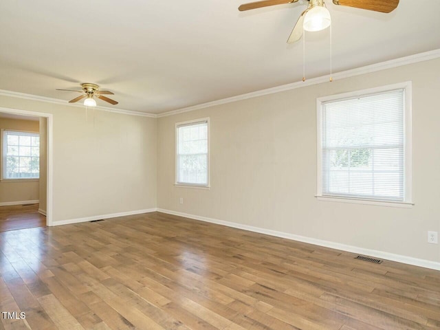 unfurnished room with a wealth of natural light, visible vents, wood finished floors, and ornamental molding