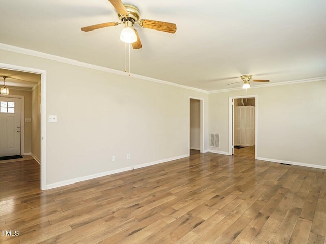 empty room featuring baseboards, visible vents, ornamental molding, and wood finished floors