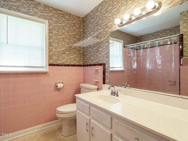 bathroom with tile walls, toilet, wainscoting, vanity, and wallpapered walls