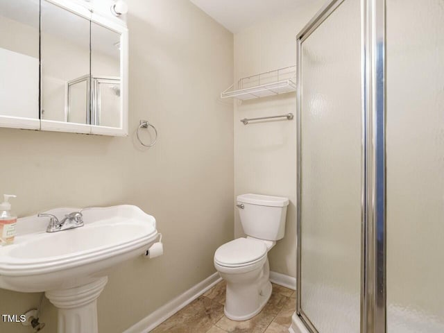 bathroom with tile patterned flooring, toilet, a sink, baseboards, and a shower stall