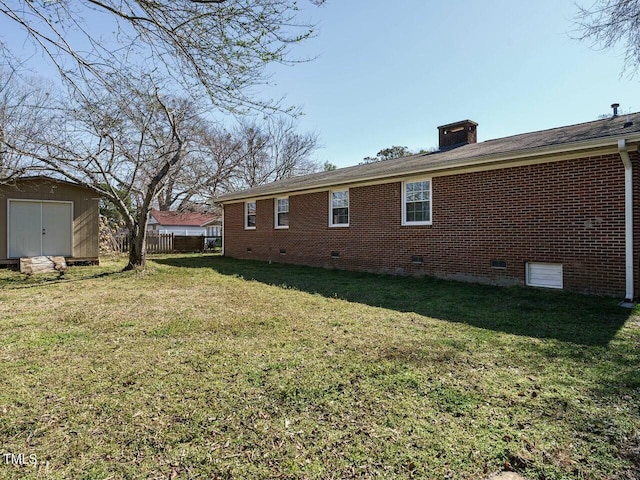 back of property featuring an outbuilding, brick siding, a yard, a storage unit, and crawl space