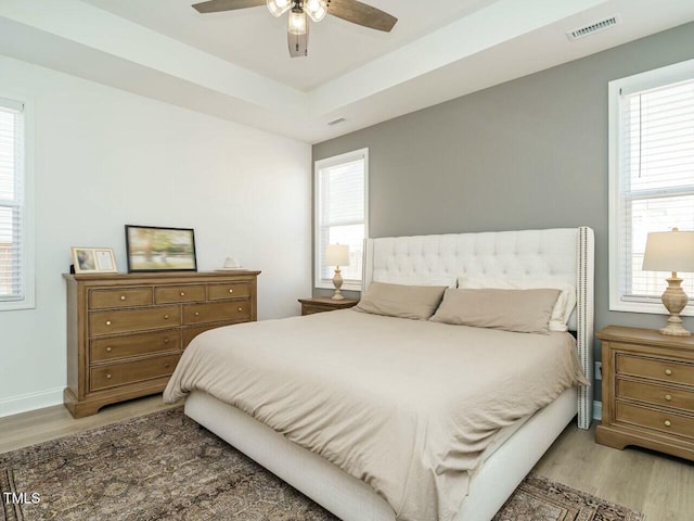 bedroom with a tray ceiling, light wood finished floors, visible vents, and baseboards