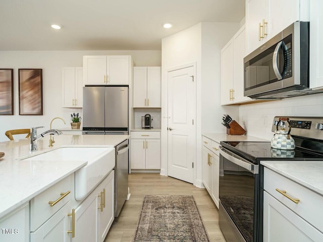 kitchen with tasteful backsplash, stainless steel appliances, light wood-type flooring, white cabinetry, and a sink