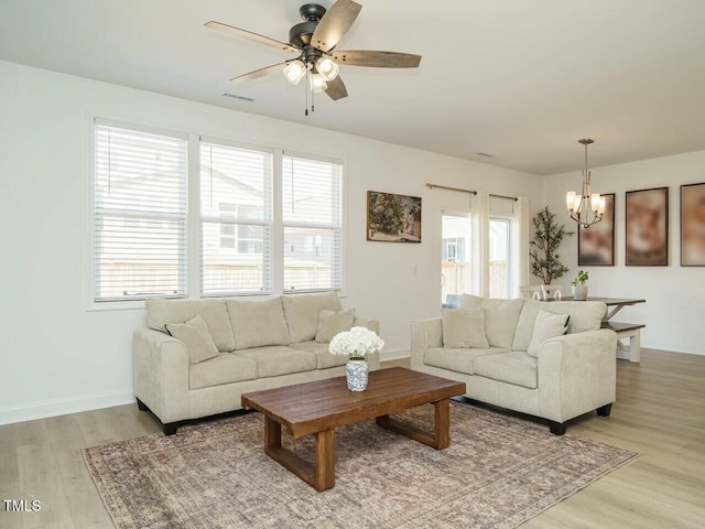 living area with baseboards, ceiling fan with notable chandelier, and light wood-style floors