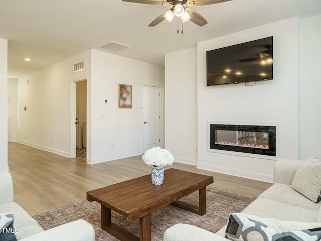 living room with a glass covered fireplace, visible vents, baseboards, and wood finished floors