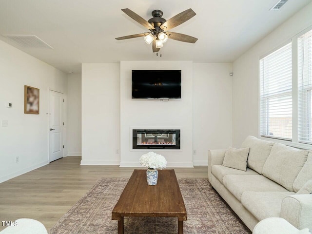 living room featuring light wood finished floors, baseboards, visible vents, and a glass covered fireplace