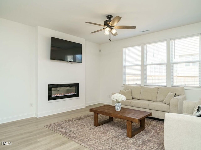 living room with visible vents, wood finished floors, a glass covered fireplace, and a wealth of natural light