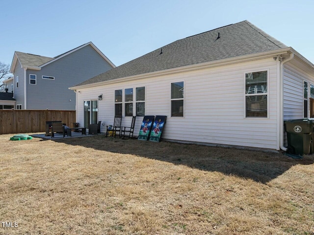 back of property featuring a patio, a shingled roof, a lawn, and fence