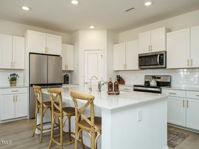 kitchen with stainless steel appliances, light wood finished floors, visible vents, and white cabinetry