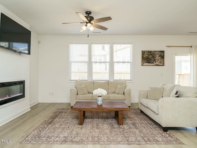 living room featuring visible vents, a ceiling fan, a glass covered fireplace, wood finished floors, and baseboards