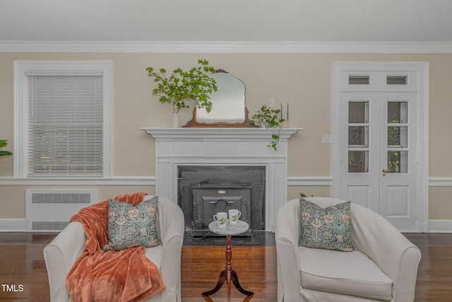 living area featuring baseboards, radiator, a fireplace with flush hearth, wood finished floors, and crown molding