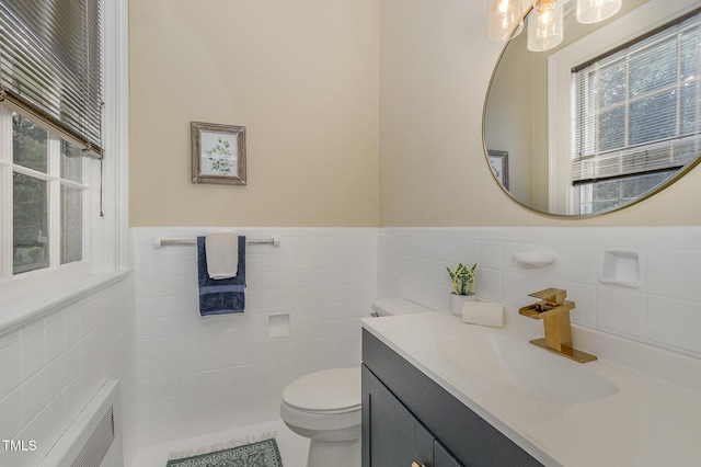 half bath with toilet, a wainscoted wall, radiator, vanity, and tile walls