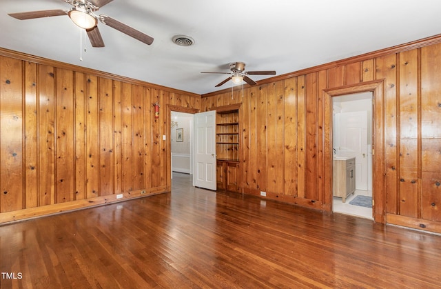 spare room with ceiling fan, wood walls, wood finished floors, visible vents, and ornamental molding