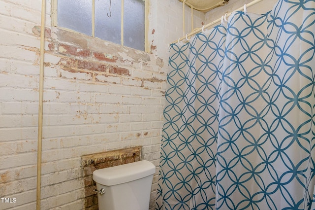 bathroom featuring toilet, curtained shower, and brick wall