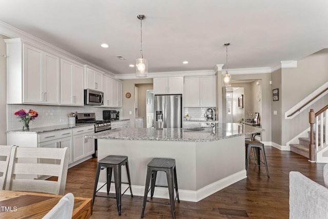 kitchen featuring a sink, white cabinets, appliances with stainless steel finishes, a kitchen bar, and a large island with sink