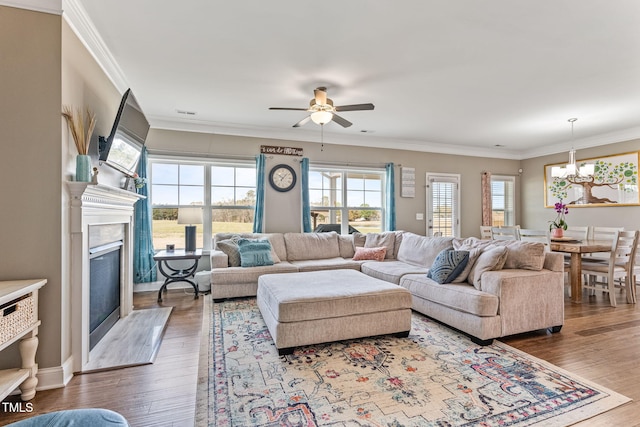 living area with ceiling fan with notable chandelier, ornamental molding, wood finished floors, and a high end fireplace