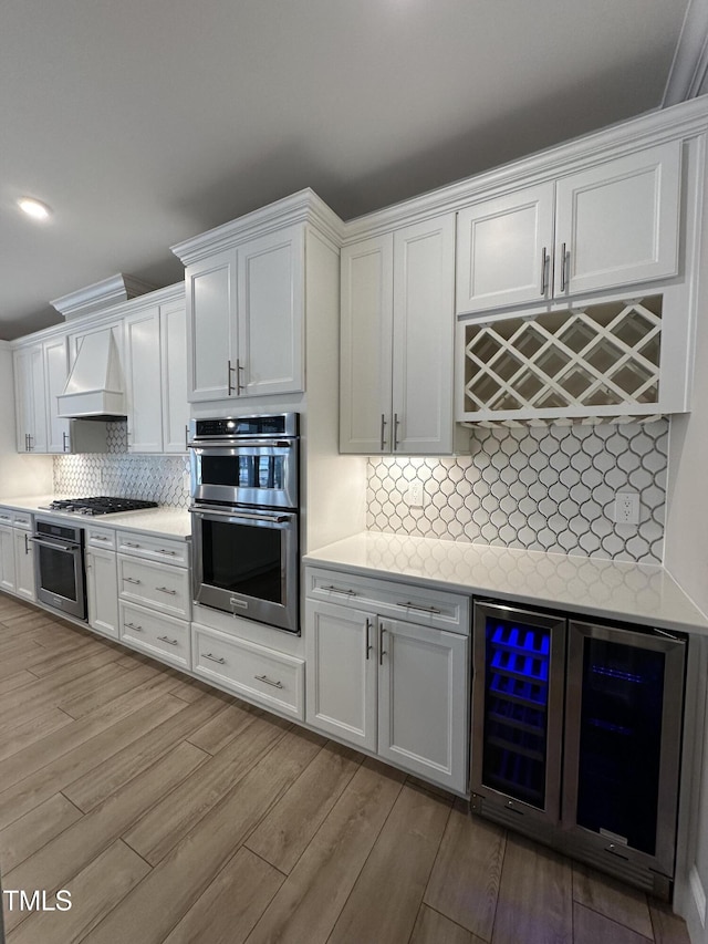 kitchen with wine cooler, white cabinetry, light countertops, appliances with stainless steel finishes, and custom range hood