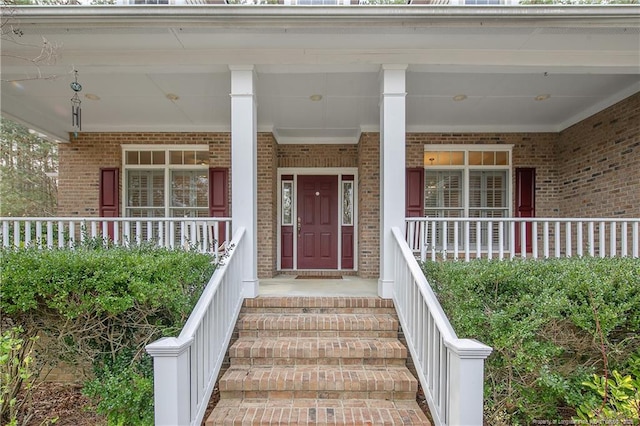 doorway to property featuring a porch and brick siding