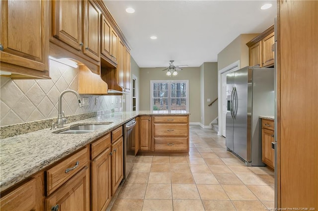 kitchen with light tile patterned floors, a peninsula, a sink, appliances with stainless steel finishes, and brown cabinetry