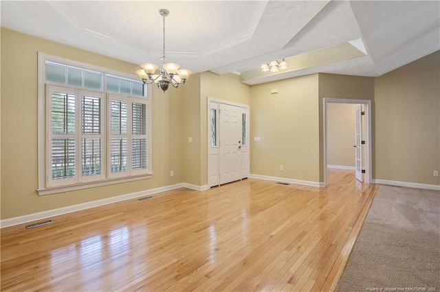 spare room featuring visible vents, baseboards, a tray ceiling, light wood finished floors, and an inviting chandelier