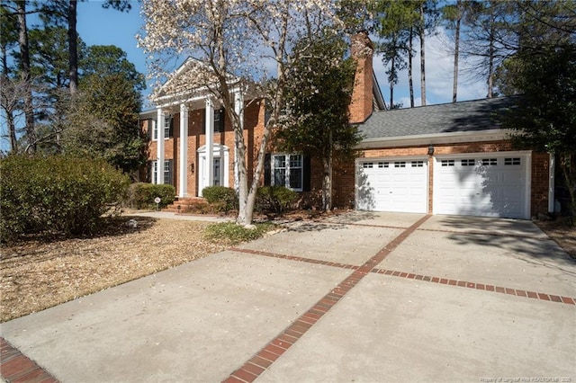 greek revival inspired property with concrete driveway, an attached garage, brick siding, and a chimney