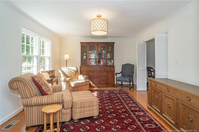 sitting room featuring light wood finished floors, visible vents, baseboards, and ornamental molding