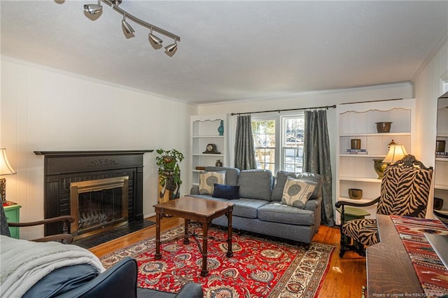 living area featuring a fireplace with flush hearth, ornamental molding, and wood finished floors