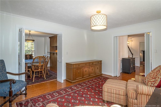 living area with a textured ceiling, wood finished floors, and ornamental molding