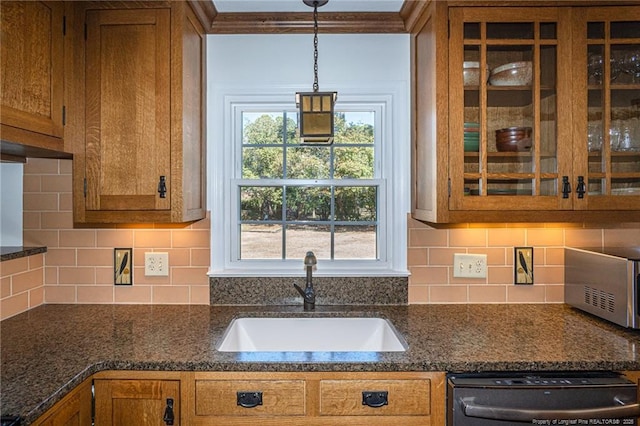 kitchen featuring tasteful backsplash, glass insert cabinets, dishwashing machine, brown cabinetry, and a sink