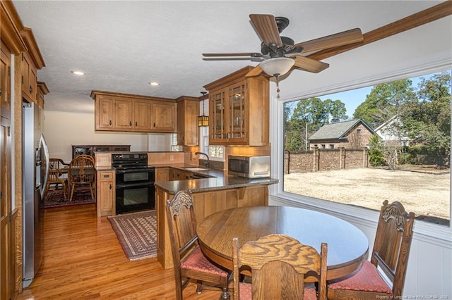 kitchen with brown cabinetry, light wood-style flooring, a sink, glass insert cabinets, and appliances with stainless steel finishes