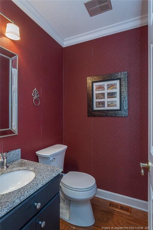 half bath with toilet, wood finished floors, visible vents, and ornamental molding