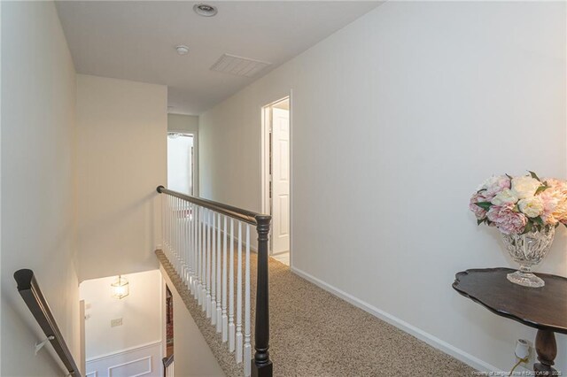 hallway featuring an upstairs landing, visible vents, baseboards, and carpet