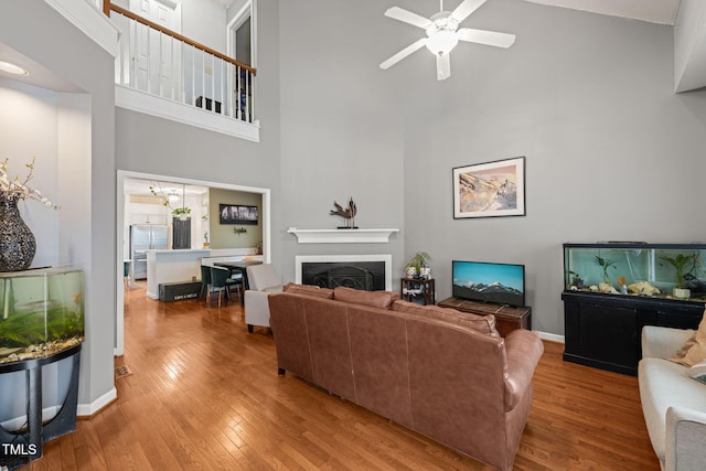 living room featuring a towering ceiling, hardwood / wood-style flooring, a fireplace, and a ceiling fan