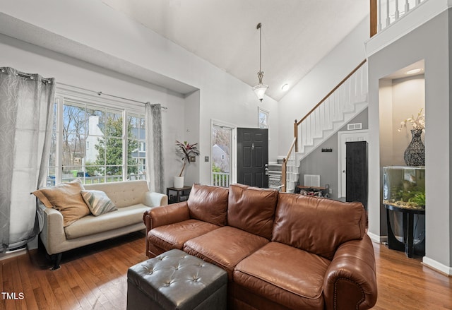 living area with high vaulted ceiling, hardwood / wood-style flooring, visible vents, and stairs