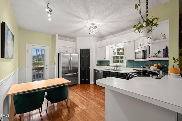 kitchen featuring light wood finished floors, open shelves, light countertops, appliances with stainless steel finishes, and a sink