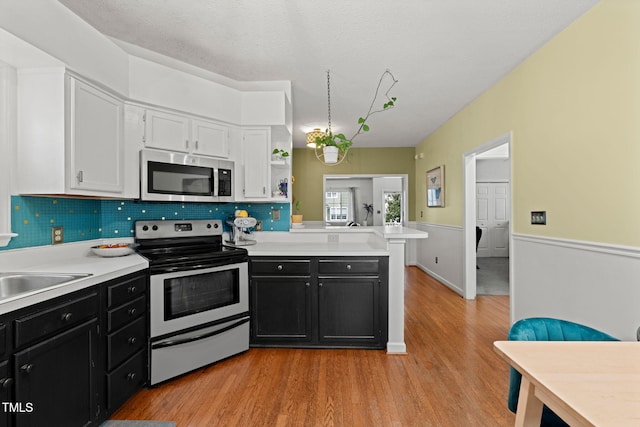 kitchen with a peninsula, appliances with stainless steel finishes, light countertops, and dark cabinets