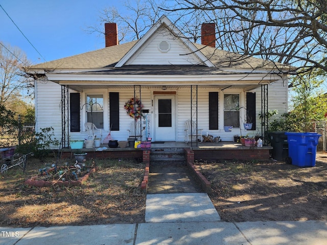 bungalow-style home featuring covered porch, a chimney, and roof with shingles