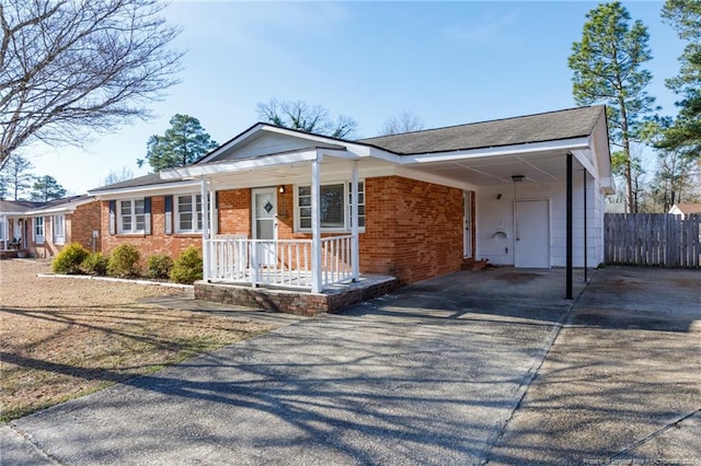 ranch-style house with aphalt driveway, a porch, an attached carport, brick siding, and fence