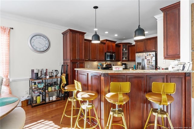 kitchen featuring reddish brown cabinets, appliances with stainless steel finishes, glass insert cabinets, wood finished floors, and a peninsula