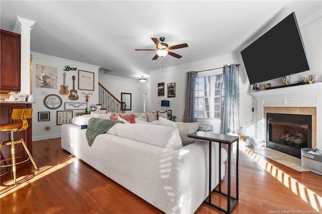 living area featuring a fireplace, a ceiling fan, ornamental molding, wood finished floors, and stairs